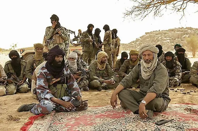 Combattants touaregs discutant sous un arbre dans un campement désertique